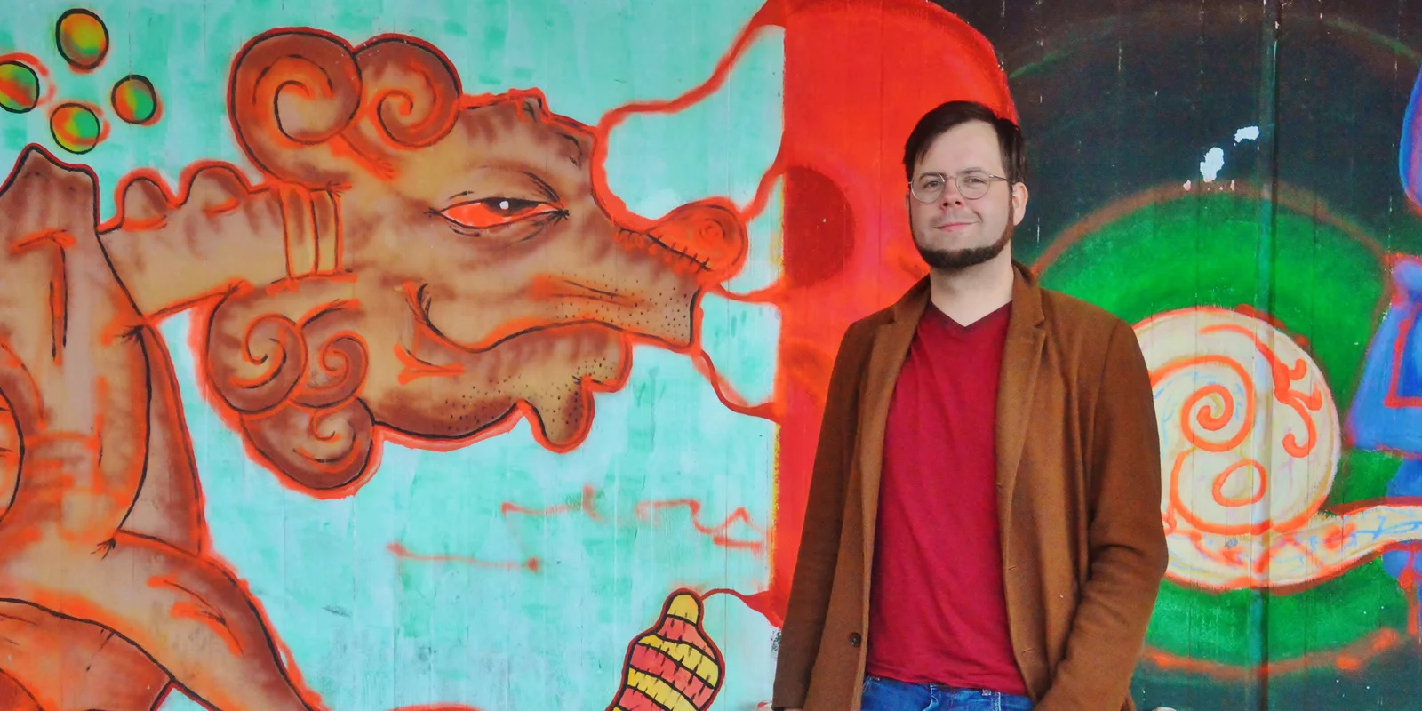 Florian Schäfer steht lächelnd vor einer Wand mit Graffiti-Kunst.
