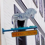 Schild mit der Aufschrift "Tiermuseum", darauf ein kleines Zebra aus Blech